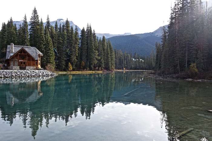 Log cabin by a lake with evergreen trees and mountains