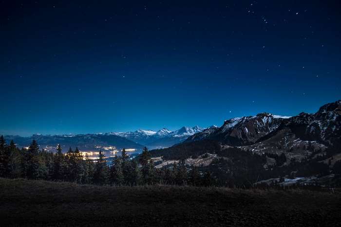 Night sky over mountains and forest with city lights