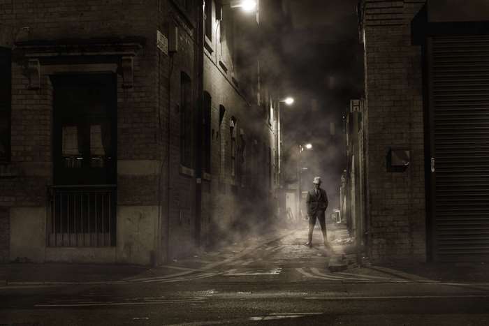 Man in a hat in a foggy alley at night