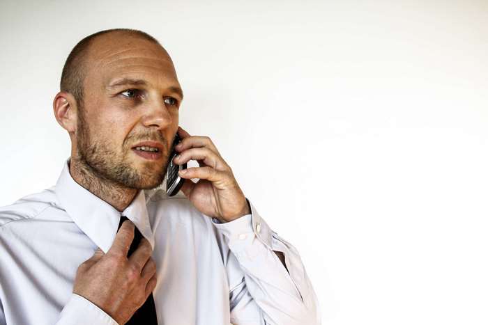 Man in white shirt talking on a mobile phone and adjusting his tie