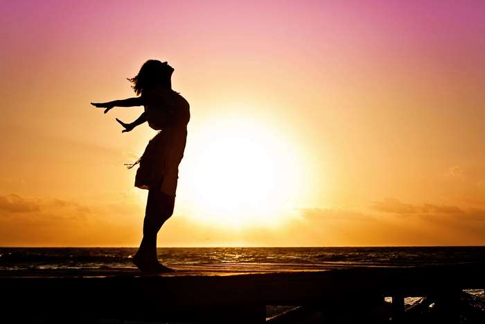 Woman in silhouette with arms outstretched at sunset