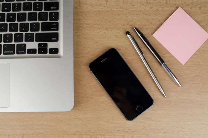 Laptop, smartphone, pens, and sticky note on a wooden desk