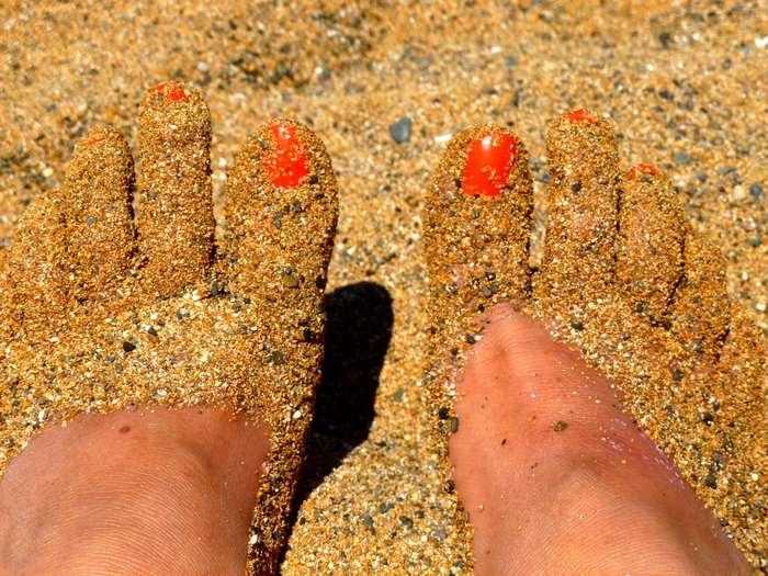Feet covered in sand with red painted toenails on a beach