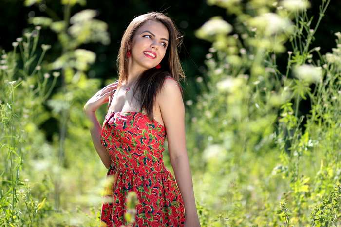 Pretty smiling girl in a red floral dress in a field