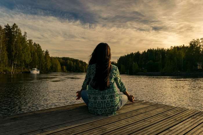 Woman meditating on a wooden dock by a lake
