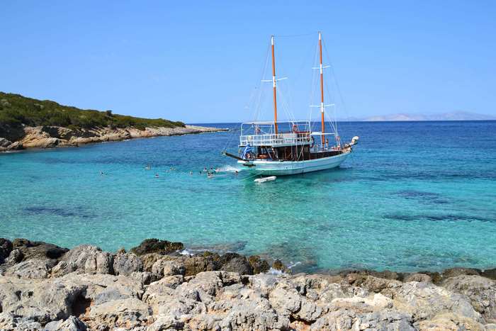 Sailing boat in a clear Mediterranean sea near a rocky shore