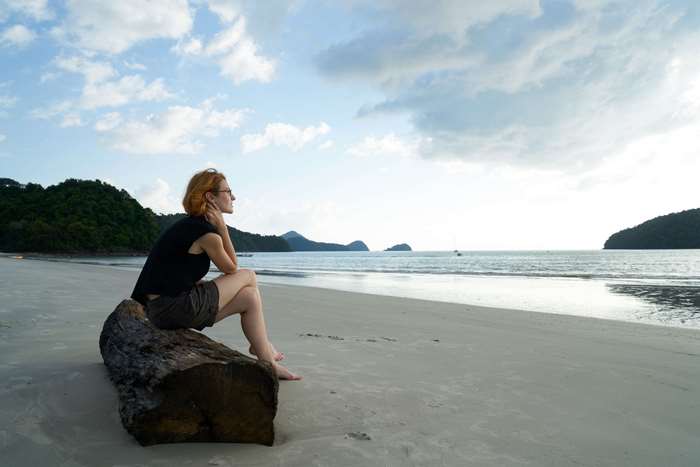 Woman sitting on a log on a beach looking out at the ocean
