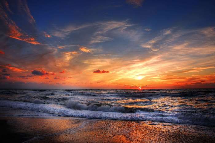 Sunset over the ocean with waves crashing on the shore