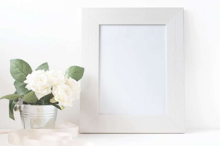 White roses in a bucket next to a white picture frame