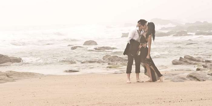 Couple kissing on a foggy beach with rocks and ocean