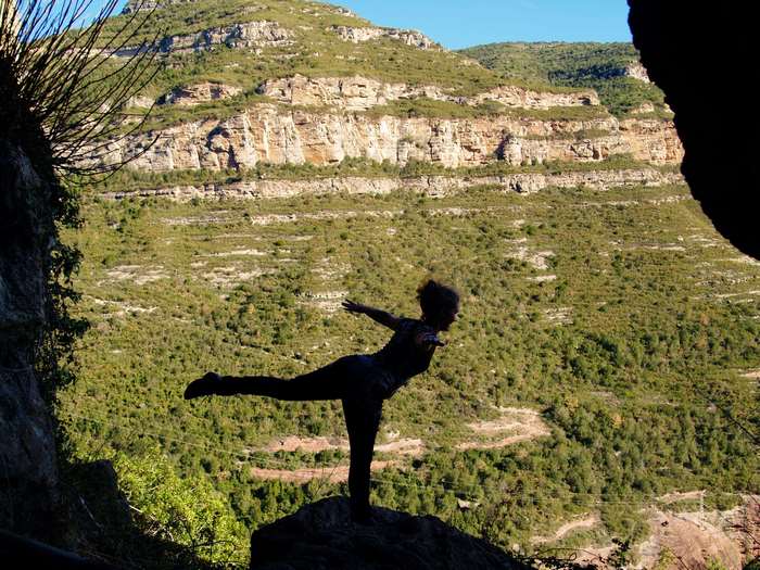 Woman practicing yoga on a rock with mountains in the background