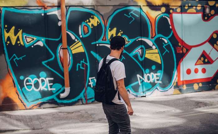 Man with backpack in front of graffiti wall