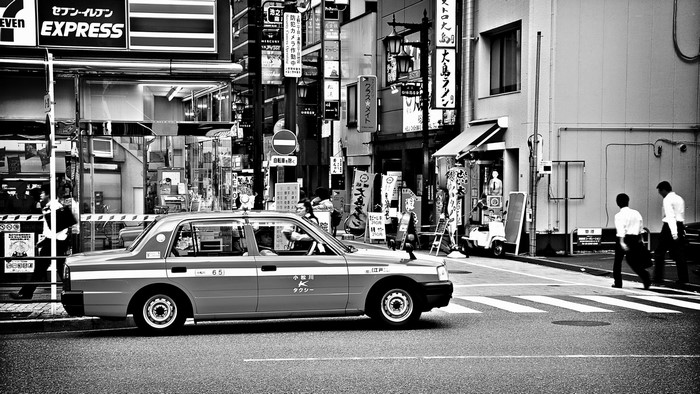Black and white street scene in Tokyo with a taxi and pedestrians