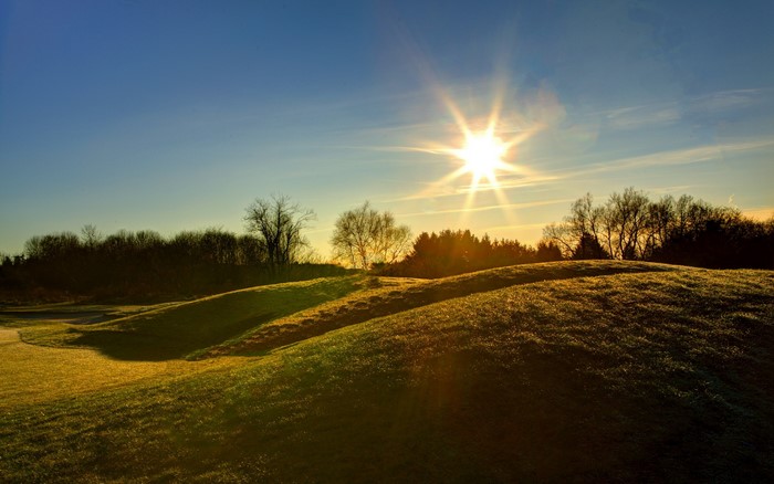 Sun shining over rolling green hills and trees