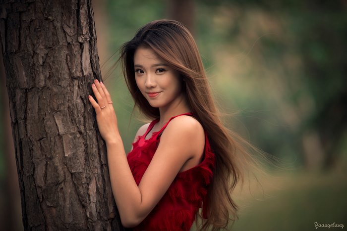 Asian woman in red dress leaning against a tree
