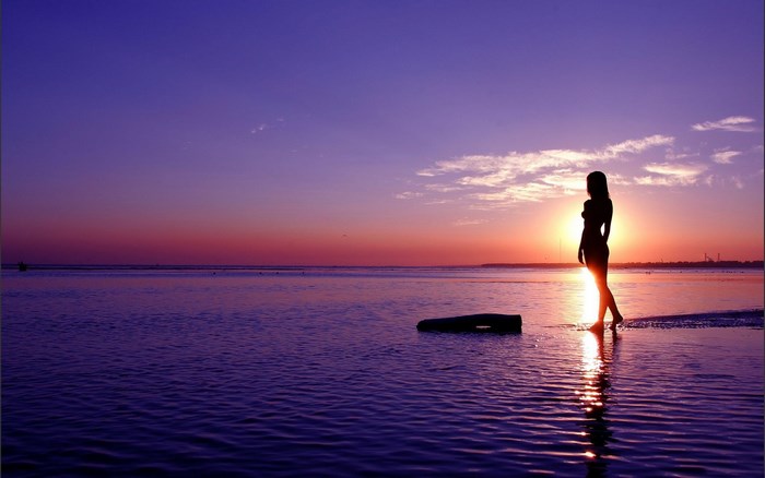Woman silhouetted against a sunset over the ocean