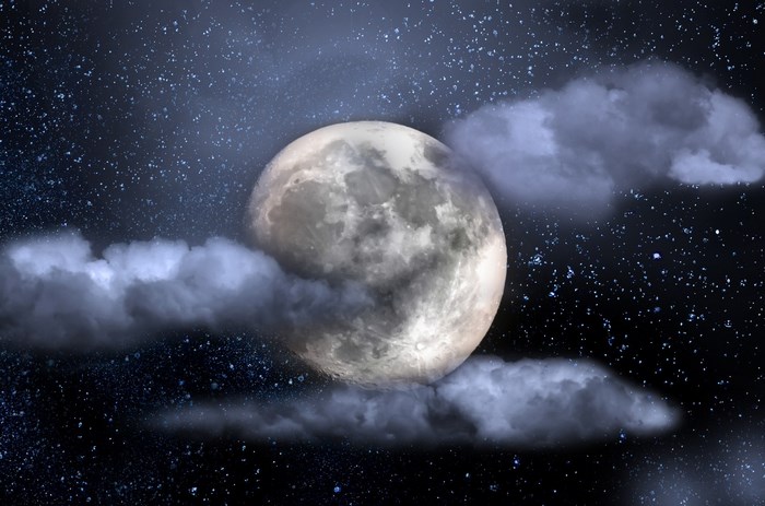 Full moon behind clouds in starry night sky