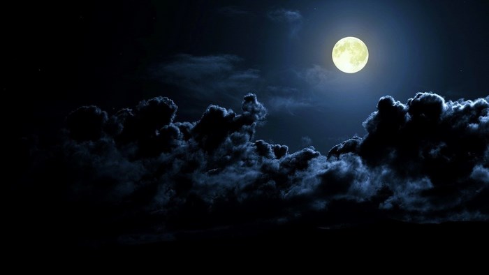 Full moon shining through dark clouds at night