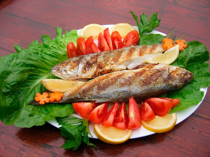 Two grilled fish with lemon and tomato garnish