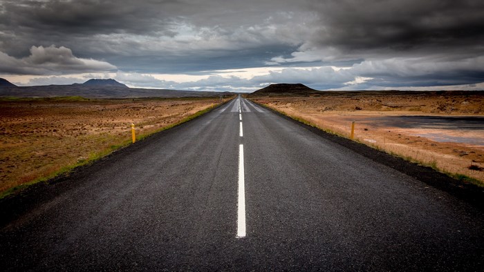 Empty road through a barren landscape under stormy clouds