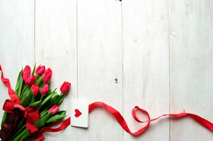 Red tulips with ribbon and card on white wood