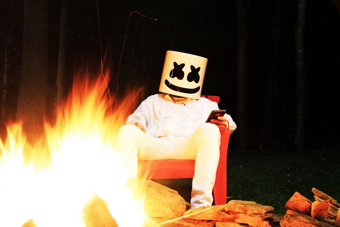 Marshmello sitting by a campfire with a phone