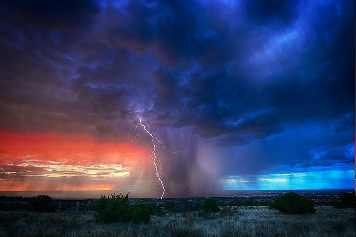Lightning strikes during a colorful sunset storm over a landscape
