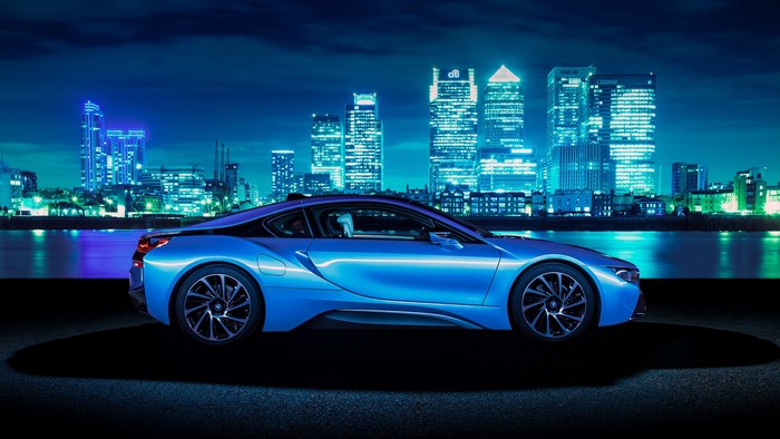 Blue BMW i8 parked by a city skyline at night