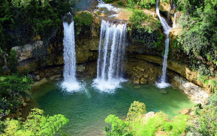 Waterfalls cascading into a turquoise pool surrounded by greenery
