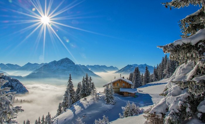 Winter mountain landscape with sun rays and a cottage
