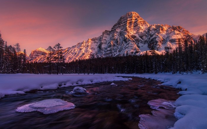 Snowy mountain peak at sunrise over a frozen river