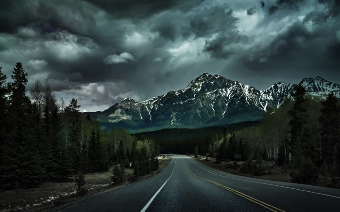 Road leading to snowy mountains under dark clouds