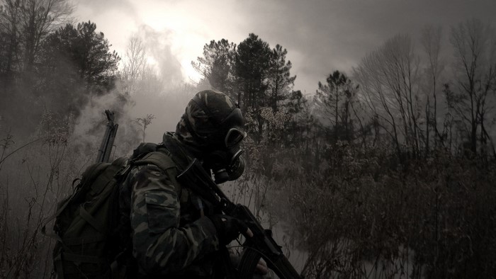 Soldier in gas mask with rifle in smoky forest