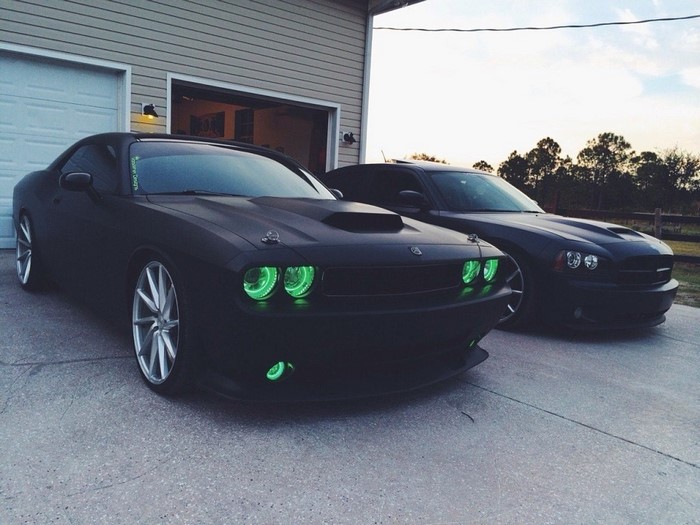 Two black Dodge cars parked outside a garage