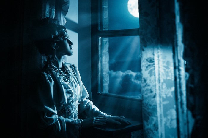 Woman in vintage dress looking out window at moon