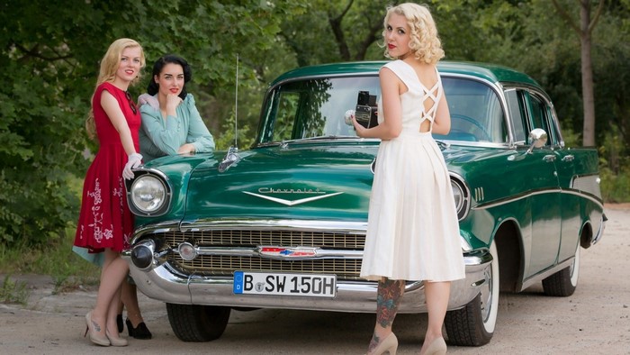 Three women in vintage dresses with a green Chevrolet car
