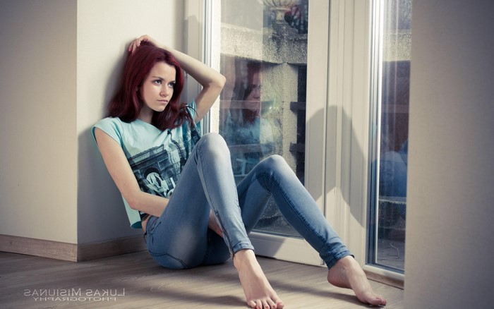 Redhead girl in jeans sitting by the window