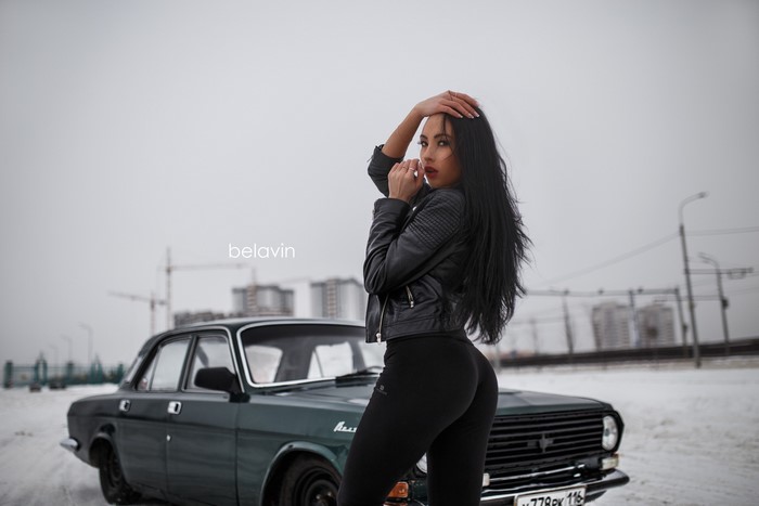 Woman in leather jacket and leggings posing by car