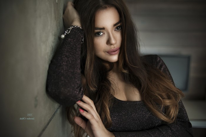 Woman with long brown hair leaning against a wall