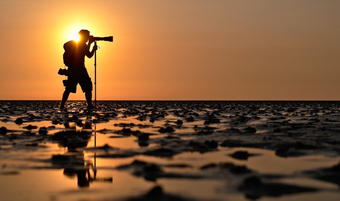 Photographer silhouetted against sunset on a beach