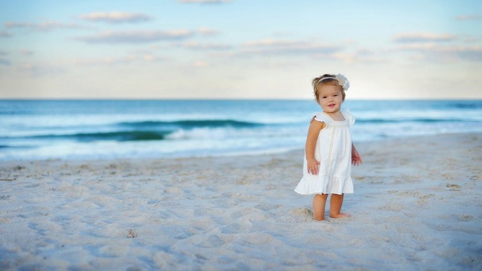 Baby girl in white dress on a beach