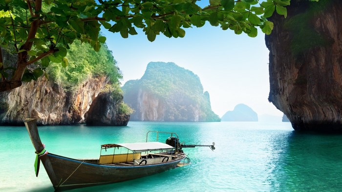Longtail boat in turquoise water near limestone cliffs in Thailand