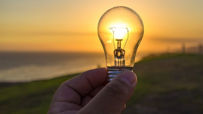 Lightbulb held against sunset over ocean