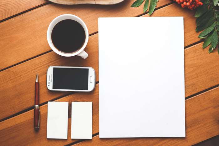 Coffee, smartphone, pen, and paper on a wooden table