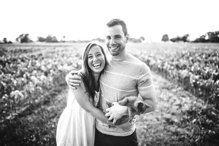 Couple laughing and holding a cat in a field