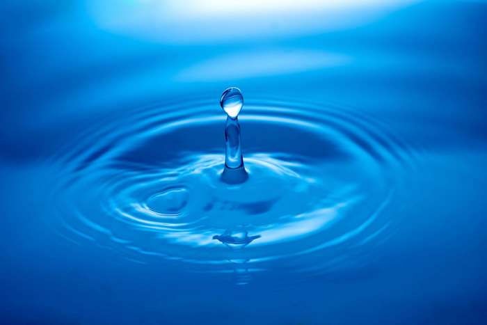 Water drop creating ripples in blue water 4K