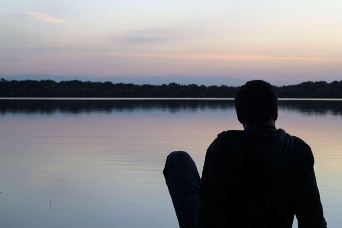 Man sitting by a lake at sunset
