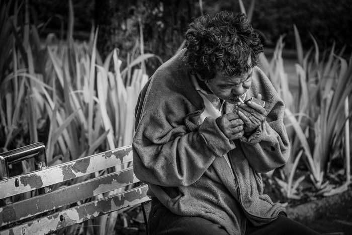 Man lighting cigarette on a park bench