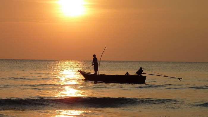 Fisherman in a boat at sunset over the ocean