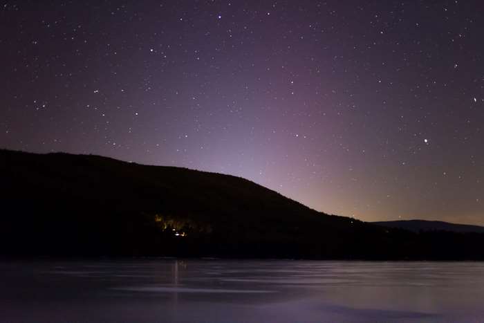 Night sky with stars over a dark hill and water
